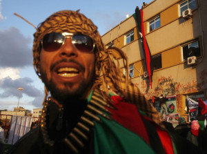 A rebel stands guard as another places a Kingdom of Libya flag at a state security building during a protest against Muammar Gaddafi in Benghazi March 8, 2011. The flag which was used when Libya gained independence from Italy in 1951, has been used as a symbol of resistance against Libya's leader Muammar Gaddafi in the recent protests. REUTERS/Suhaib Salem (LIBYA - Tags: POLITICS CIVIL UNREST CONFLICT)